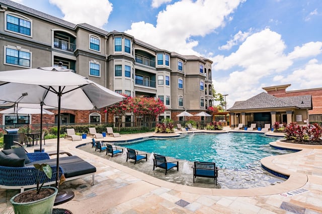 Luxury apartment complex pool area with lounge chairs and umbrellas.