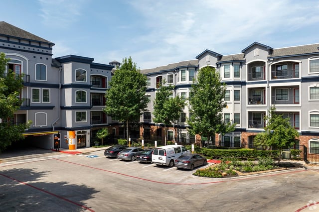 Exterior view of a multifamily apartment building with parking lot and landscaping.