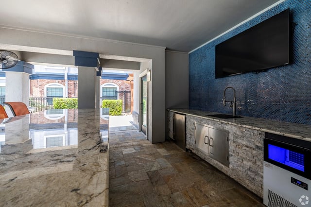 Outdoor kitchen and entertainment area with a granite countertop, sink, outdoor TV, and ice maker.