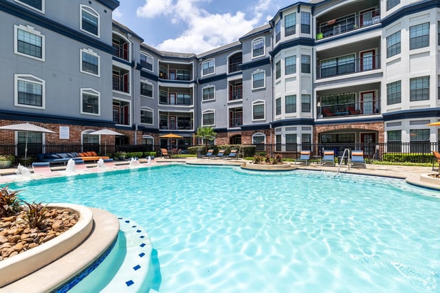Apartment complex swimming pool with lounge chairs and fountains.