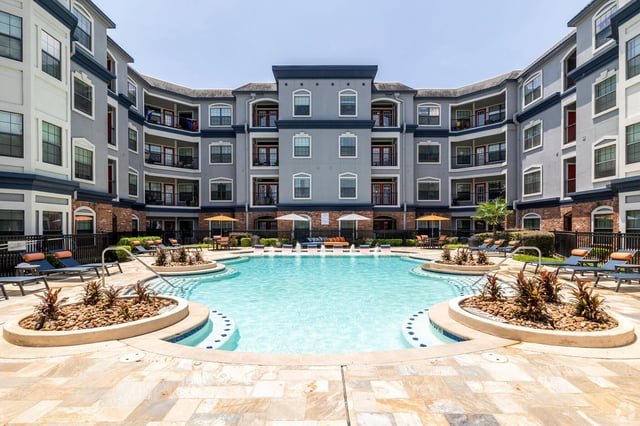 Swimming pool with lounge chairs and umbrellas in front of apartment buildings.