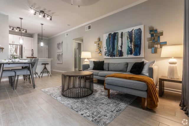A living room with a grey sectional sofa, coffee table, dining table, and kitchen counter.