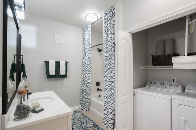 Modern bathroom with vanity, tub, shower, and in-unit washer and dryer.