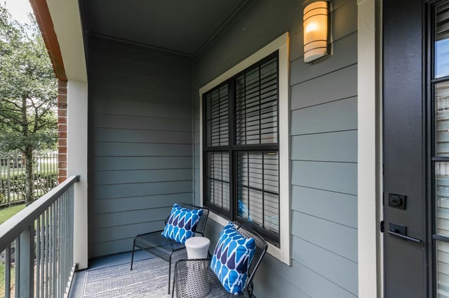 Balcony with two chairs and decorative pillows, featuring a window and outdoor lighting.