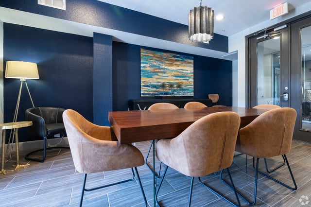A communal dining table with chairs in a room with blue walls and modern art.