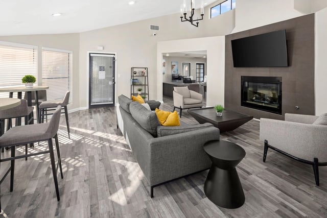 Stylish community lounge area with modern sofas, armchairs, a coffee table, fireplace, and TV.