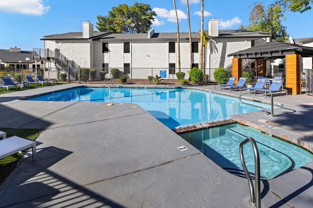 Outdoor swimming pool and hot tub with lounge chairs and a covered seating area.