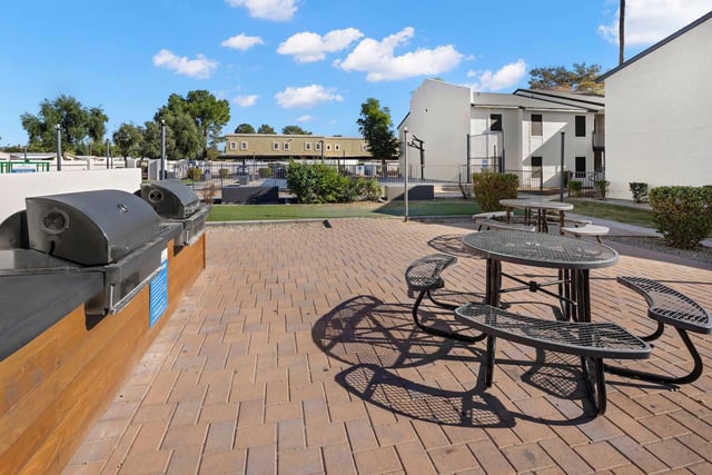 Outdoor grilling area with multiple built-in grills and picnic tables on a paved patio.