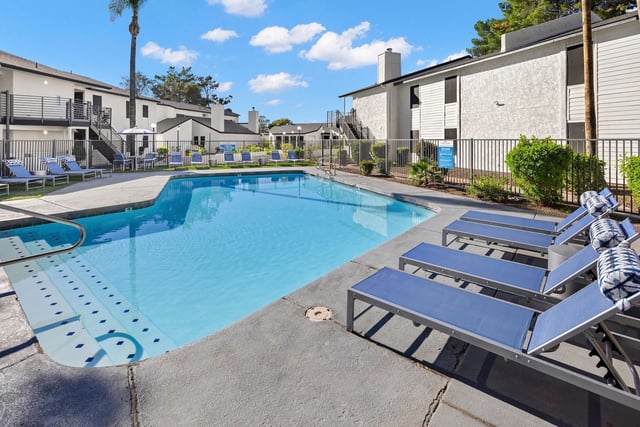 Resort-style swimming pool with lounge chairs and surrounding apartment buildings.