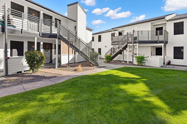 Exterior view of apartment buildings with outdoor staircases and a central grassy courtyard.