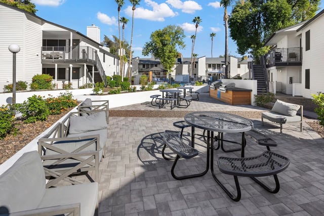 Outdoor patio area with picnic tables, grills, and seating near apartment buildings.