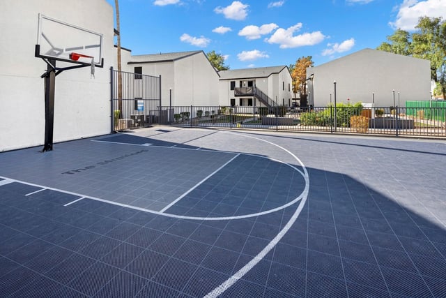 Outdoor basketball court with a hoop and buildings in the background.