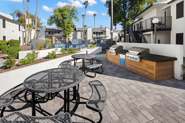 Outdoor seating area with grills and a swimming pool in the background.