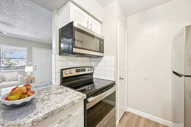 Modern kitchen with granite countertops, stainless steel appliances including a microwave and refrigerator, and white cabinetry.