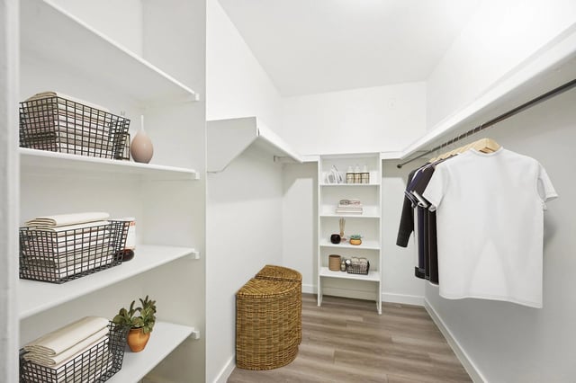 Walk-in closet with white shelves, baskets, and hanging clothes.