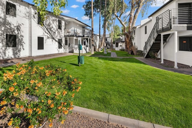 Apartment buildings surrounding a grassy courtyard with blooming orange flowers and mature trees.