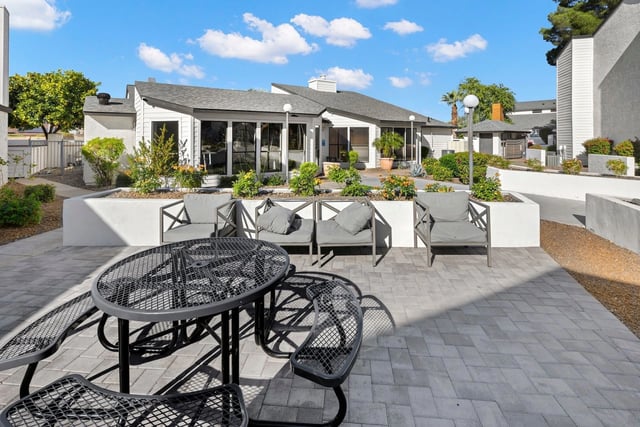 Outdoor patio seating area with tables and chairs, adjacent to a building with large windows.