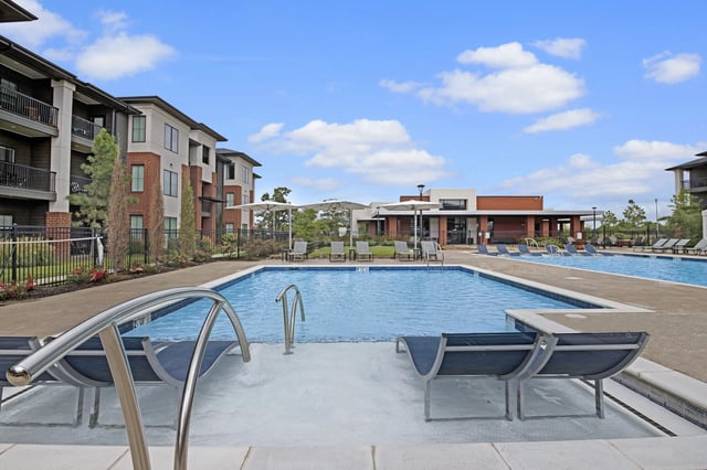 Luxury swimming pool with lounge chairs and apartment buildings in the background.