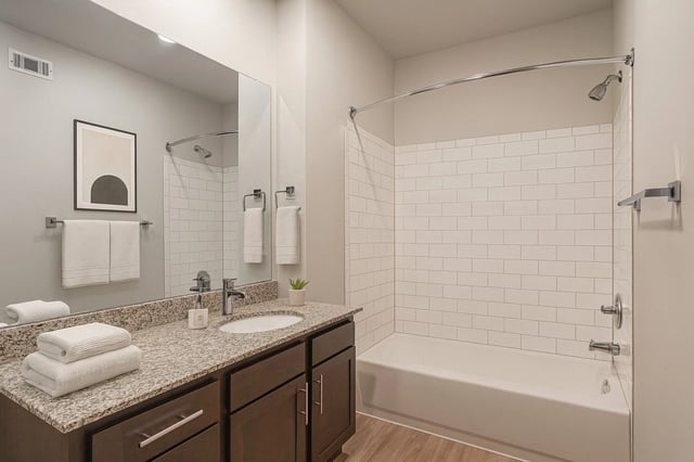 Modern bathroom with a granite countertop, dark wood vanity, and white subway tile shower.