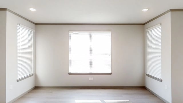 Empty living room with neutral walls, blinds on windows, and light wood floors.