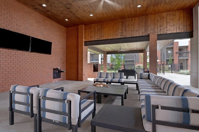 Outdoor lounge area with seating and tables, featuring brick walls and wood ceilings.
