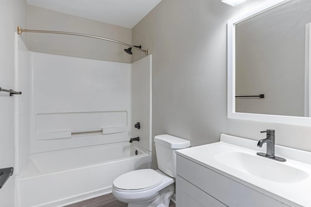Modern bathroom with white vanity, sink, faucet, toilet, and bathtub with shower.
