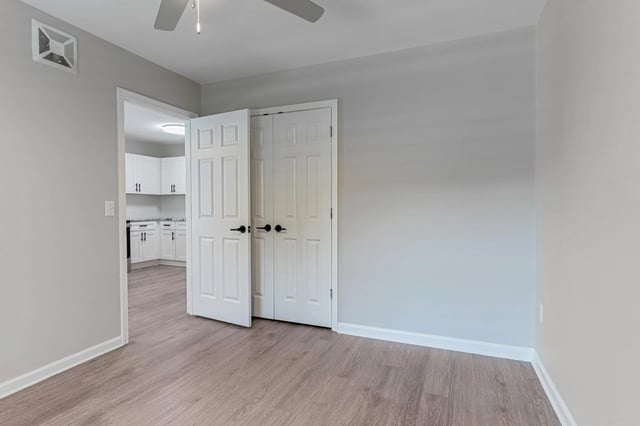 View of a bedroom with light grey walls, a ceiling fan, and a closet with double doors.