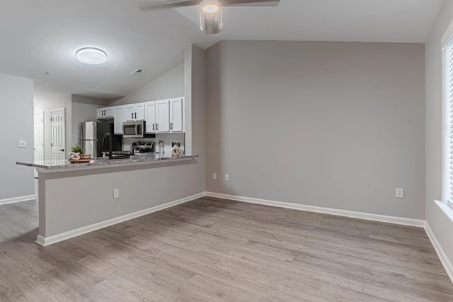 Open-concept living area and kitchen with a kitchen island, white cabinets, and a ceiling fan.