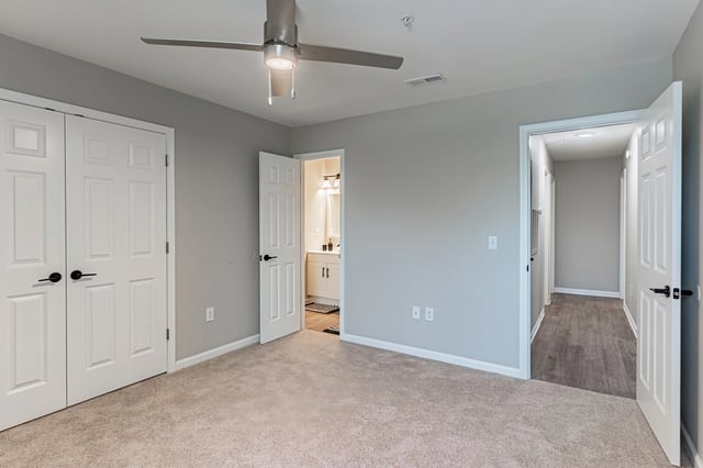 Bedroom with ceiling fan, double closet doors, and view into a bathroom.