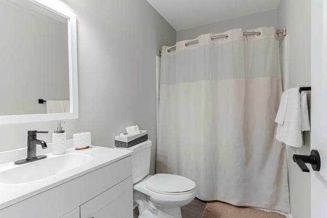 Modern bathroom with a white vanity, black faucet, and a beige shower curtain.