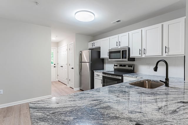 Modern kitchen with stainless steel appliances, white cabinets, and a granite countertop.