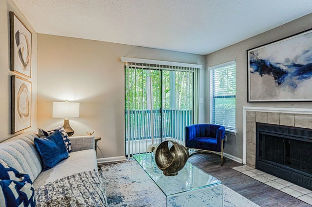 Modern living room with a gray sofa, blue accent chair, glass coffee table, and fireplace.