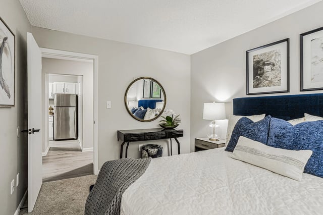 Bedroom with a navy blue headboard, white comforter, and blue accent pillows. A console table with a mirror is visible.