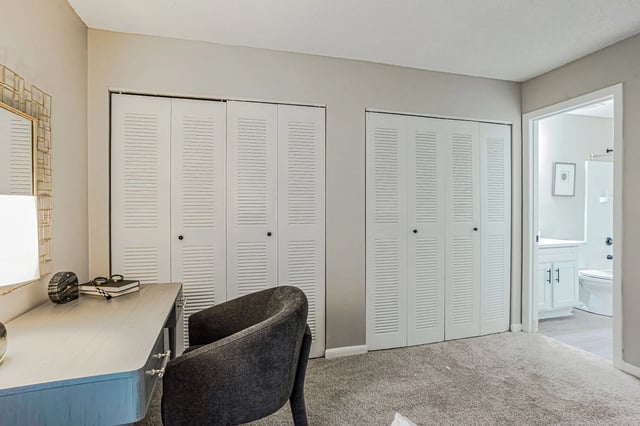 Dressing area with a desk, chair, and closet doors. A bathroom is visible through an open doorway.
