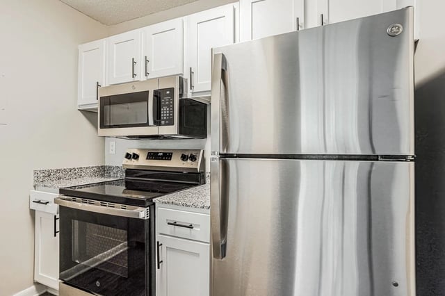 Stainless steel refrigerator and microwave above an electric stove in a modern kitchen.