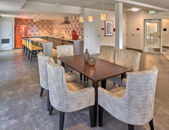 Dining area with chairs and table in front of a kitchen with orange refrigerator.