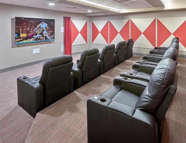 Home theater with rows of reclining leather seats and a large screen displaying a football game.