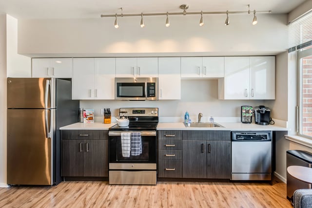 Modern kitchen with stainless steel appliances, white and gray cabinetry, and hardwood floors.