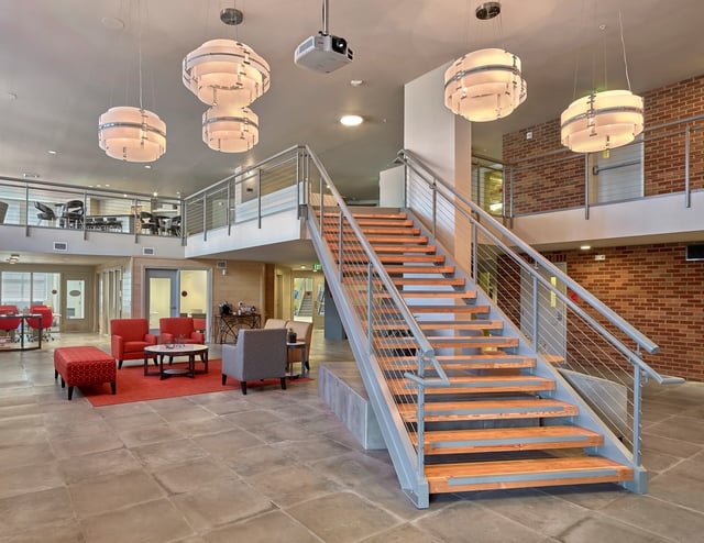 Modern staircase with wood treads and metal railings in a bright, open common area with seating.
