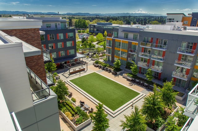 Modern apartment complex courtyard with artificial turf, seating areas, and mountain views.