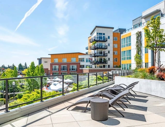 Rooftop lounge area with chaise lounges and outdoor seating, overlooking a courtyard and apartment buildings.