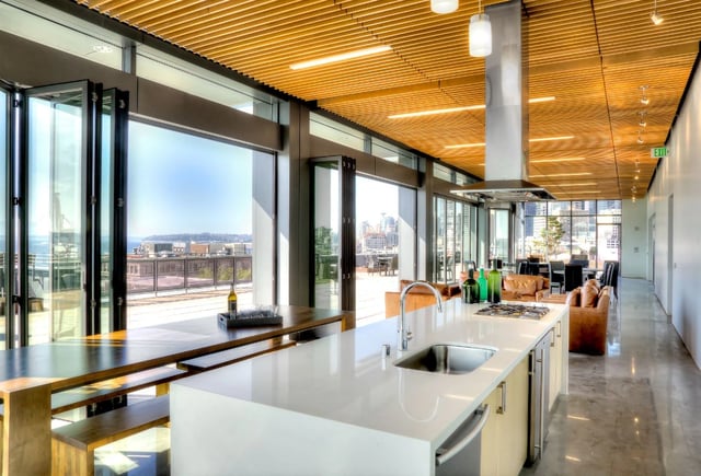 Modern community kitchen with island, bar seating, and folding glass doors leading to an outdoor patio with city views.