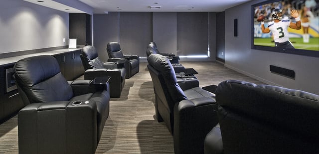 Theater room with recliners and large screen showing a football game.