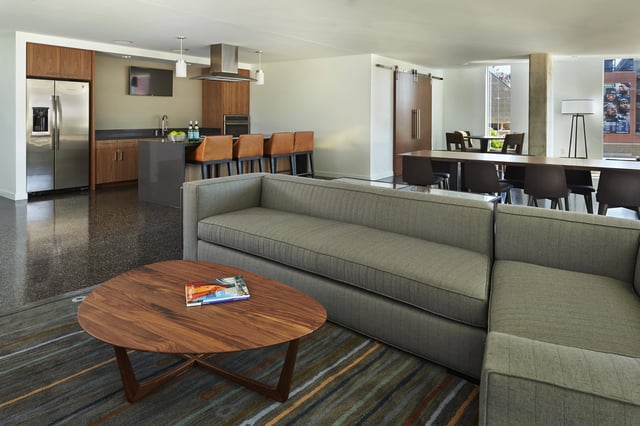 Sleek modern communal lounge area with a full kitchen, bar seating, and a large dining table.