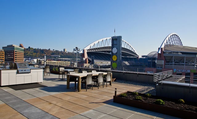 Rooftop patio with outdoor kitchen and seating overlooking a stadium