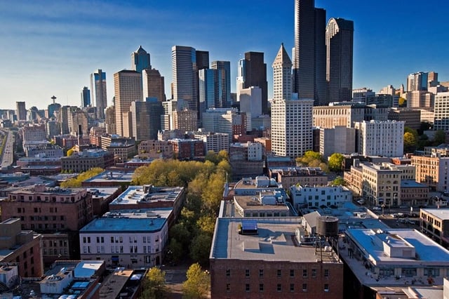 Aerial view of a dense urban cityscape with tall skyscrapers and smaller buildings below, under a clear blue sky.