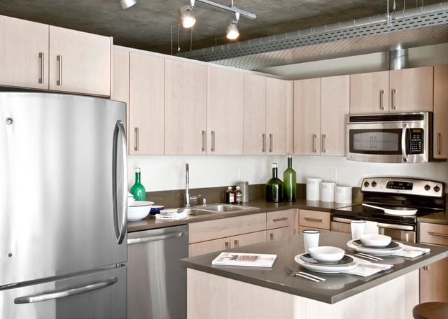 Modern kitchen with stainless steel appliances, light wood cabinets, and a granite island.