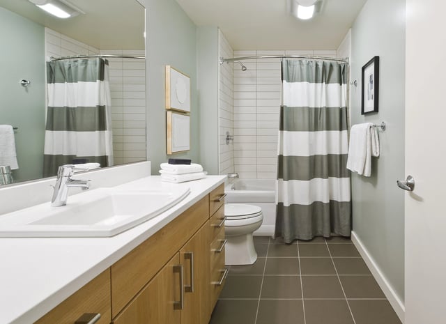 Modern bathroom with a double vanity, toilet, and shower-tub combo with a striped curtain.