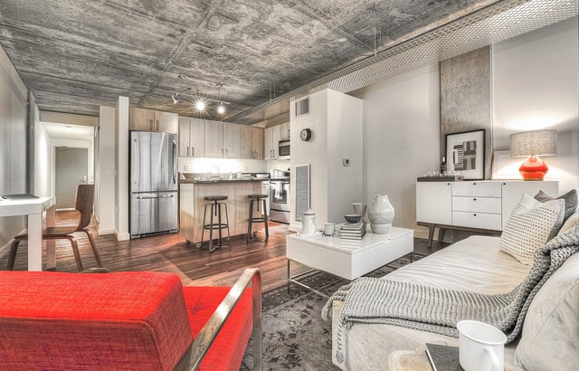 Living room and kitchen in a modern apartment with concrete ceilings and stainless steel appliances.