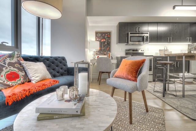 Stylish living room and kitchen area with a blue tufted sofa, striped armchair, and modern dark wood cabinets.